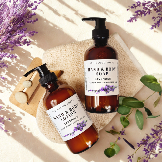 Two bottles of lavender hand and body products on a light background with lavender flowers.