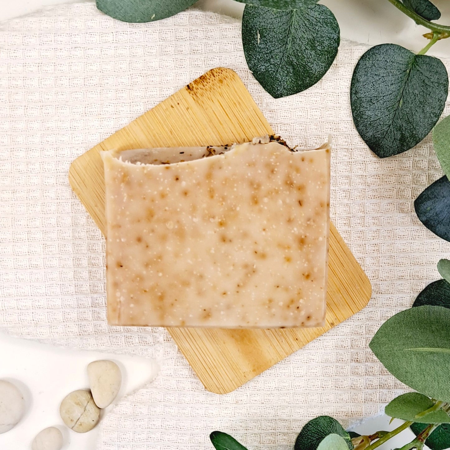 Bar of soap on a wooden board with green leaves and stones on a textured surface