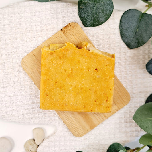 Yellow soap bar on a wooden board with green leaves in the background