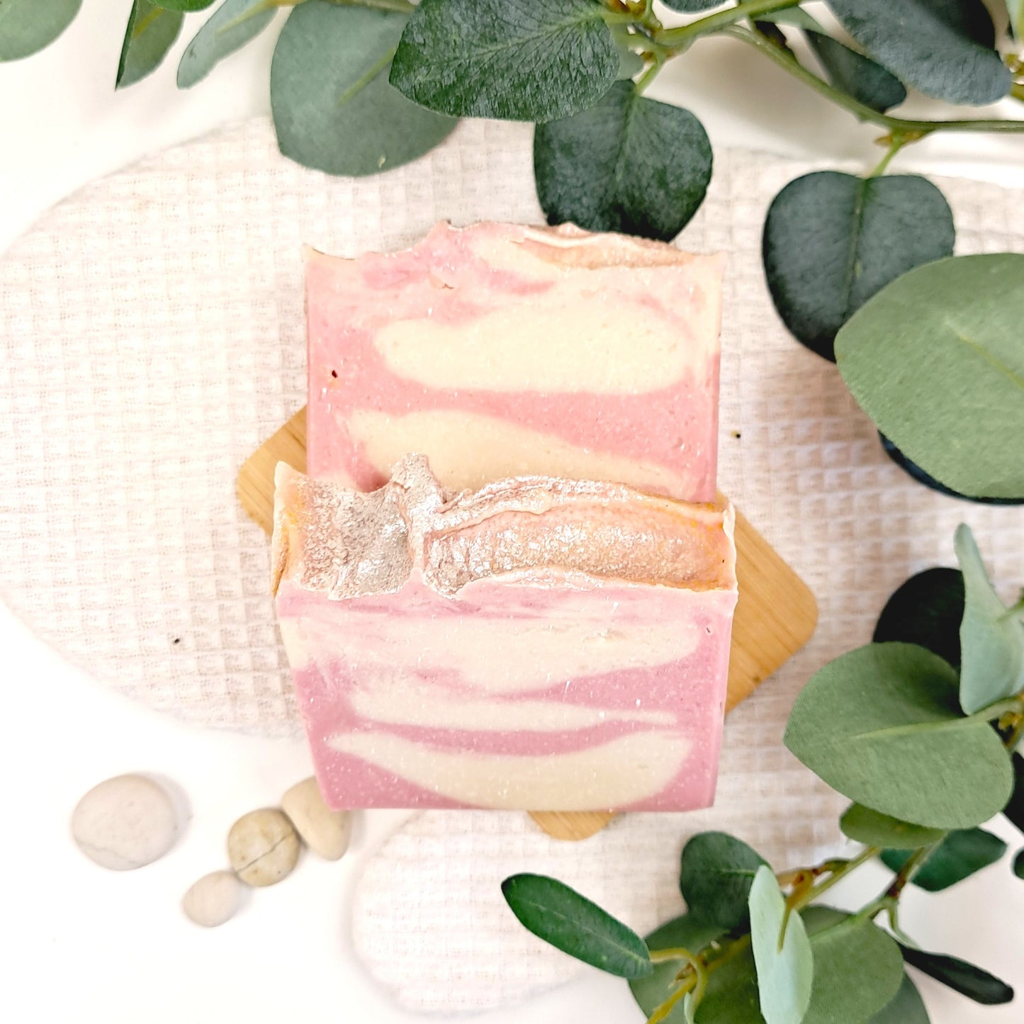 Bar of soap with pink and white swirls on a white surface with green leaves