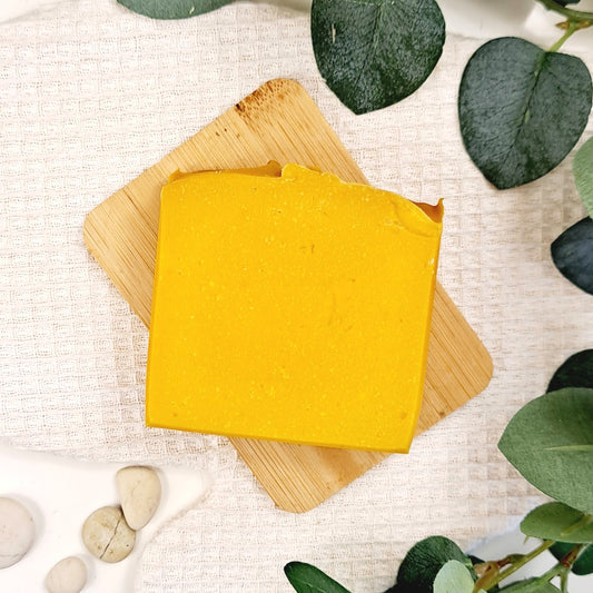 Yellow soap bar on a wooden board with green leaves and stones on a textured surface