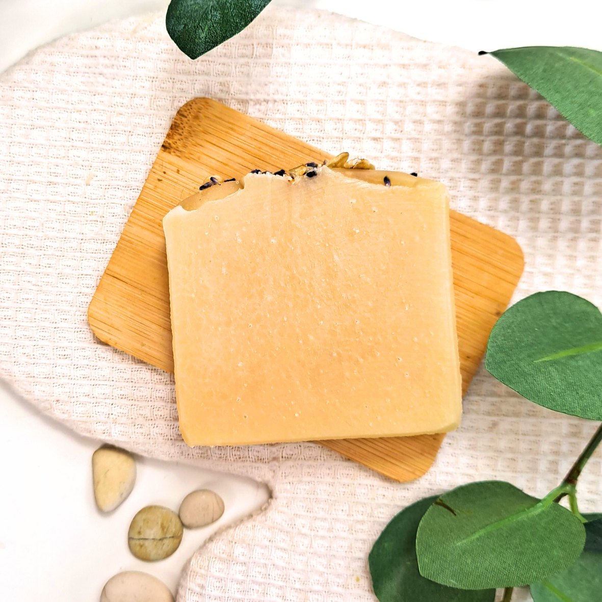 Two yellow soap bars on a textured surface with green leaves and stones