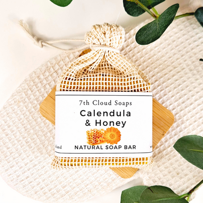 7th Cloud Soaps Calendula & Honey natural soap bar in a mesh bag with green leaves on a white background
