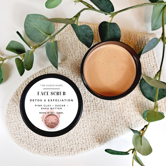 7th Cloud Soaps Face Scrub container with a lid on a textured surface with green leaves.