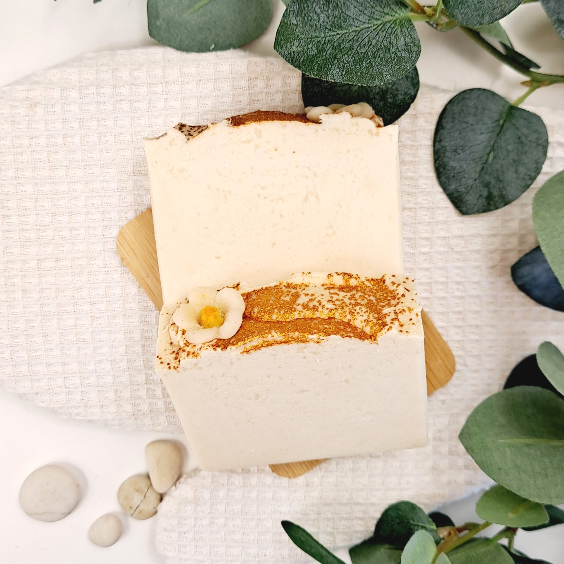 Two soap bars with gold accents on a white textured surface with green leaves.