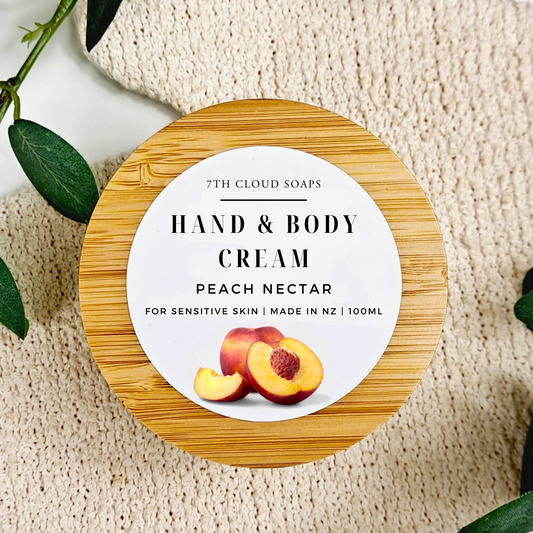 Hand and body cream container with peach nectar flavor on a textured surface with green leaves.