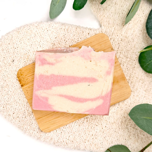 Pink and white soap bar on a wooden board with green leaves in the background
