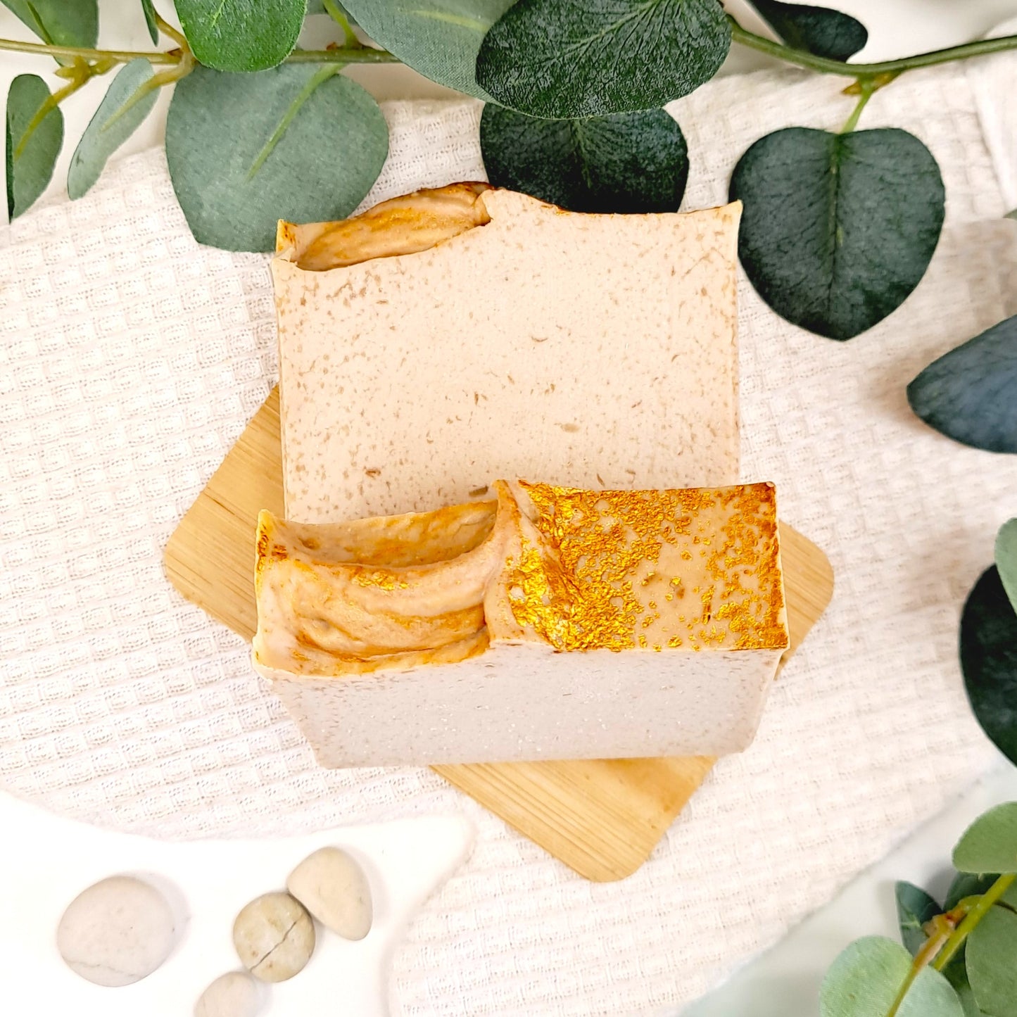 Two soap bars on a wooden stand with green leaves in the background