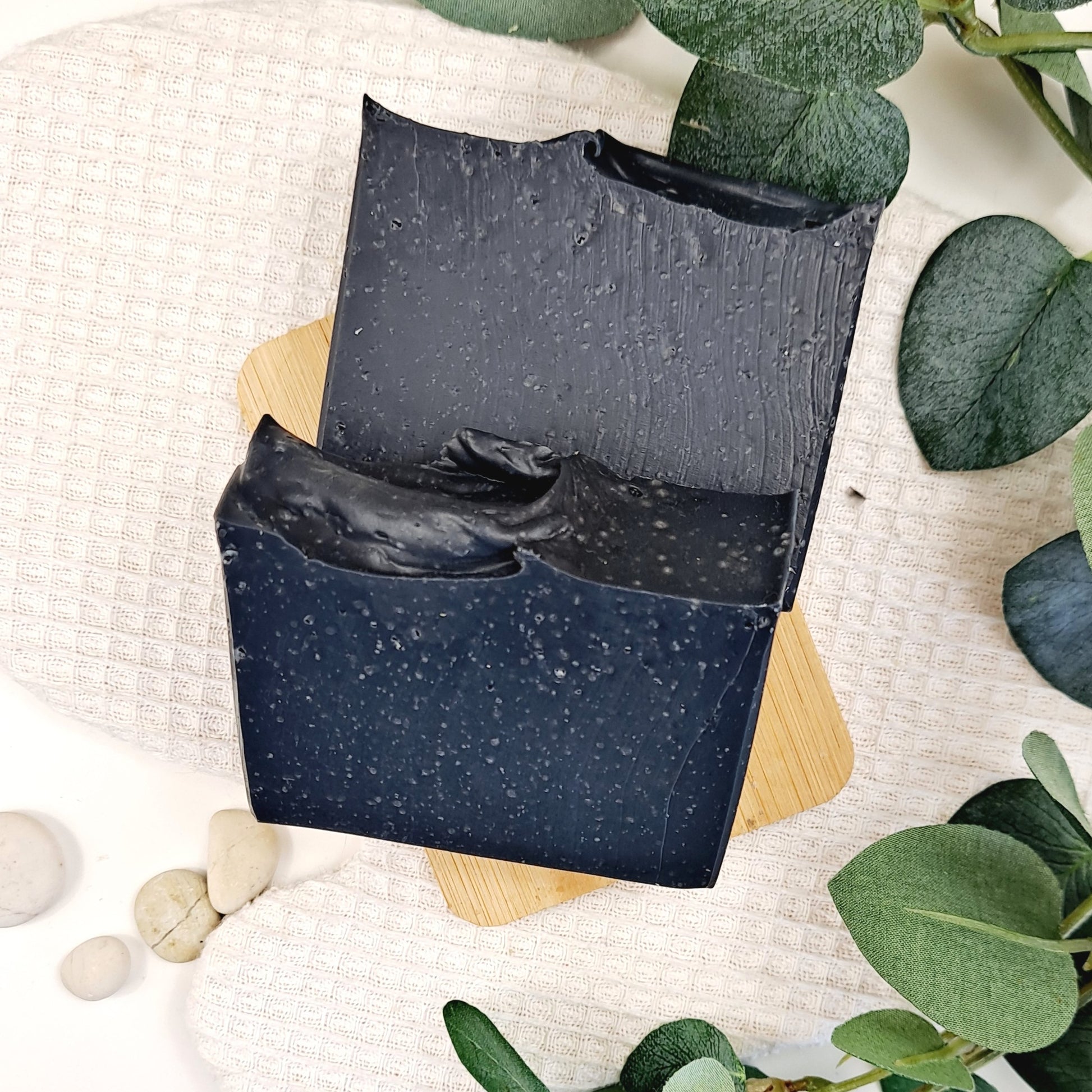 Black soap bar with a textured surface on a light background with green leaves.