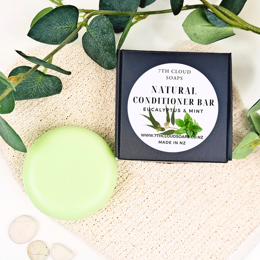Green natural conditioner bar with packaging labeled '7th Cloud Soaps' on a textured surface with eucalyptus leaves.
