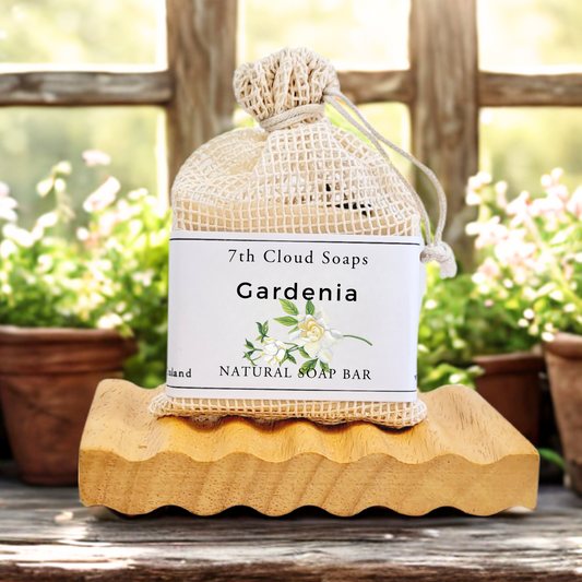 Gardenia soap bar in a mesh bag on a wooden block with plants in the background