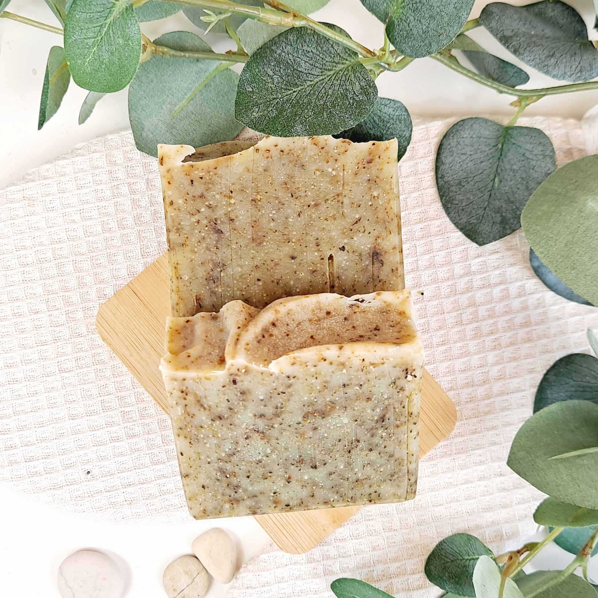 Three bars of natural soap on a wooden block with green leaves in the background