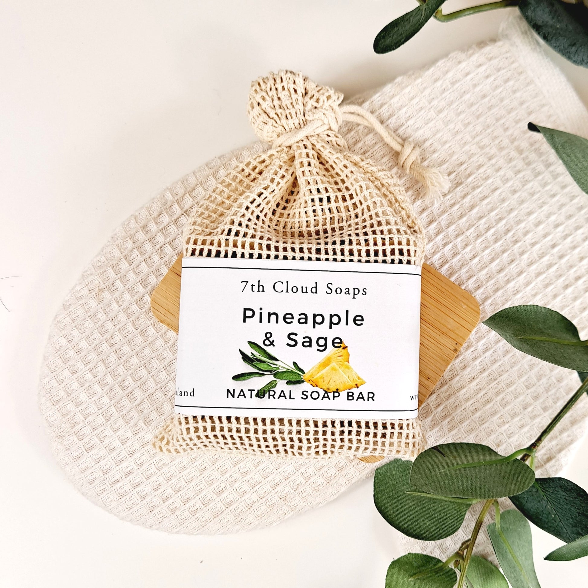 A natural soap bar labeled 'Pineapple & Sage' from 7th Cloud Soaps, placed in a burlap sack, with eucalyptus leaves in the background.