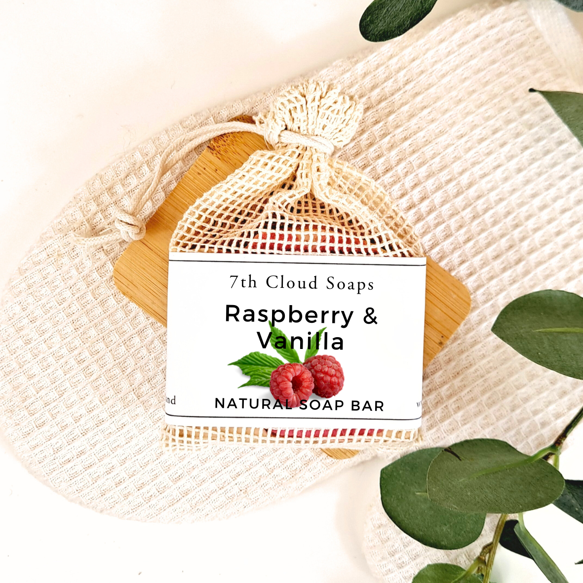 7th Cloud Soaps Raspberry & Vanilla natural soap bar in a mesh bag on a textured surface with green leaves.