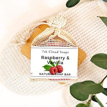 7th Cloud Soaps Raspberry & Vanilla natural soap bar in a mesh bag on a textured surface with green leaves.