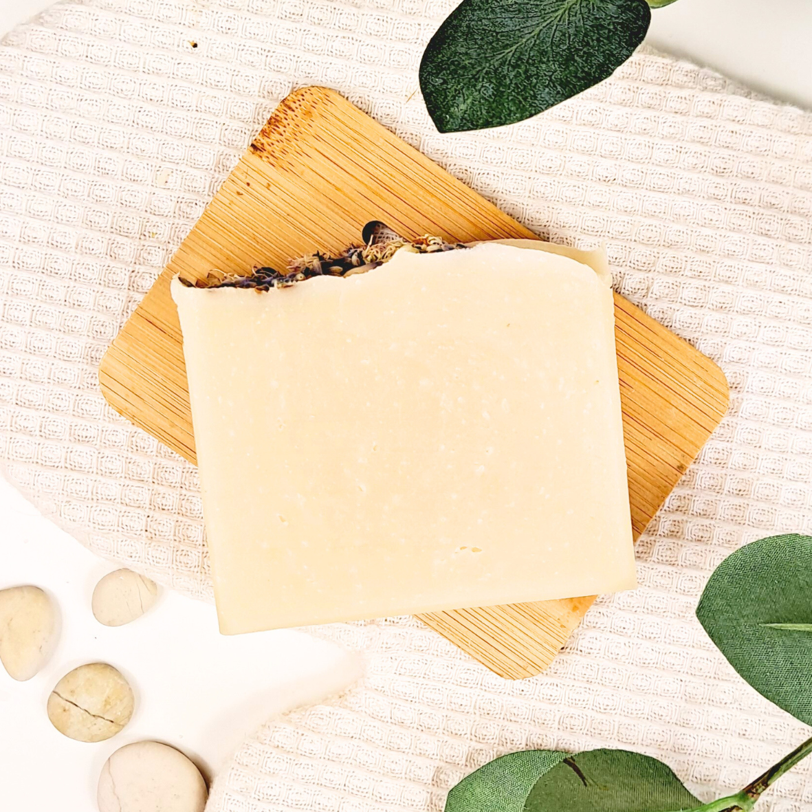 Bar of soap on a wooden soap dish with leaves and stones on a textured surface