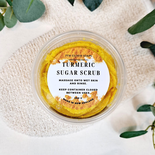 A jar of Turmeric Sugar Scrub placed on a white cloth with leaves in the background.