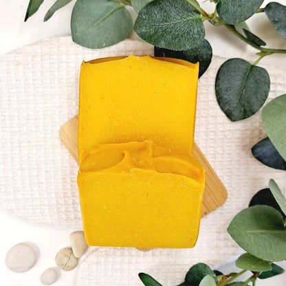 Yellow soap bar on a wooden soap dish with green leaves and stones in the background