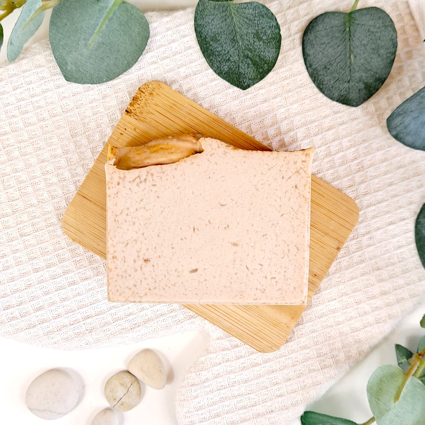 Bar of soap on a wooden soap dish with eucalyptus leaves on a textured white background